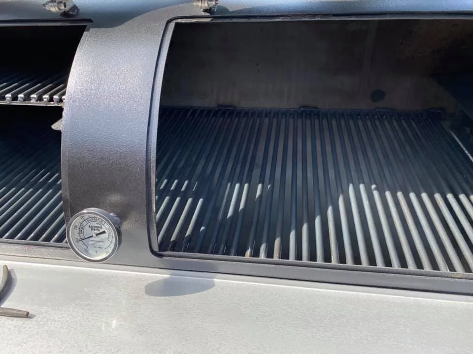 Close-up of an open Jambo cook chamber showing heavy grates and a temperature gauge